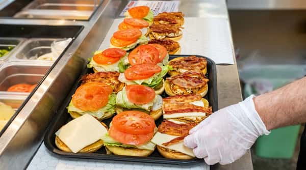 An assembly line of burgers and bacon sandwiches on a tray, topped with lettuce, tomato, and cheese.
