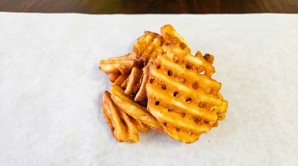 A pile of golden-brown waffle fries, some ridged and some flat, on white parchment paper.