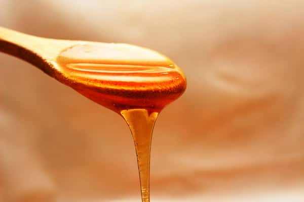 Golden honey slowly drizzling from a wooden spoon against a warm, softly lit background.