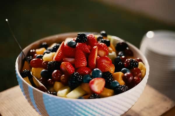 A bowl of fresh fruit salad with strawberries, blackberries, grapes, blueberries, and melon chunks served with a spoon.