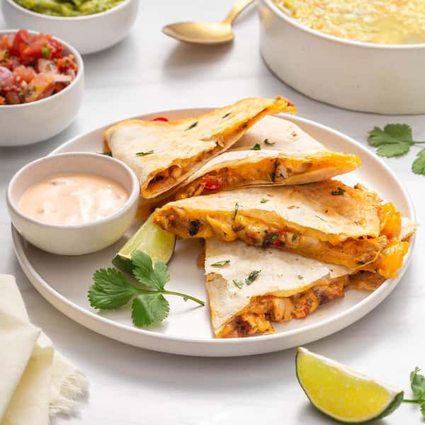 Quesadillas filled with chicken, peppers, and cheese, served with creamy dressing and Mexican side dishes on a white plate.