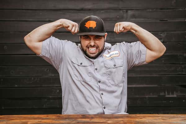 man in branded hat showing off "guns" (muscles)