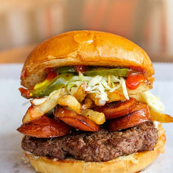 Loaded beef burger topped with grilled sausage, crispy fries, pickles, shredded cabbage, and signature sauce on a toasted brioche bun at Social Burger.