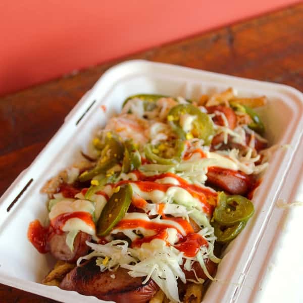 Loaded fries topped with grilled sausage, shredded cheese, jalapeños, and signature sauces, served in a takeout container at Social Burger.