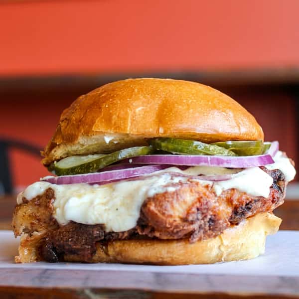 Grilled chicken sandwich topped with melted cheese, pickles, red onions, and creamy garlic sauce on a toasted brioche bun at Social Burger.