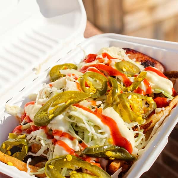Loaded fries topped with grilled sausage, shredded cheese, jalapeños, and signature sauces, served in a takeout container at Social Burger.