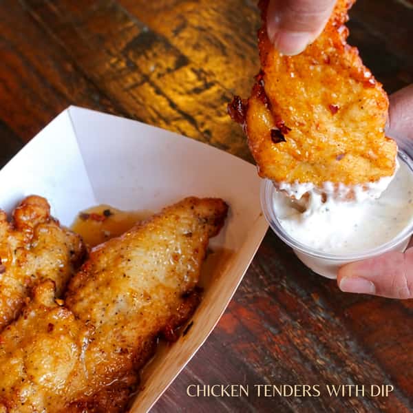 Crispy Social Burger chicken tenders served with creamy ranch dipping sauce, featuring a hand dipping a tender into the sauce.