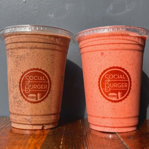 Two handcrafted Social Burger milkshakes in branded cups, featuring rich chocolate and strawberry flavors served fresh on a wooden table.