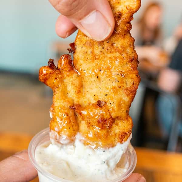 Hand dipping a crispy Social Burger chicken tender into creamy ranch sauce for the perfect bite.