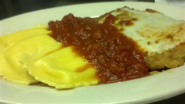 Breaded chicken topped with melted mozzarella cheese and a side of raviolis topped with red marinara sauce.