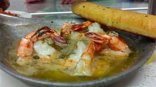 Shrimp in a dish of butter with a garlic bread stick.