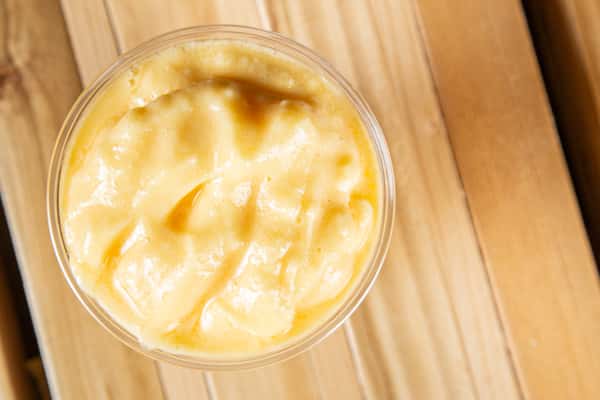 Tropical mango smoothie or fruit blend with a creamy texture and ice, captured from above in a clear cup on a rustic wooden table, highlighting a refreshing café beverage.