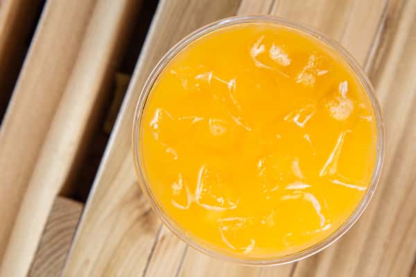 Bright iced mango or tropical fruit drink with ice cubes in a clear cup, captured from above on a wooden table, evoking a refreshing summer café beverage.