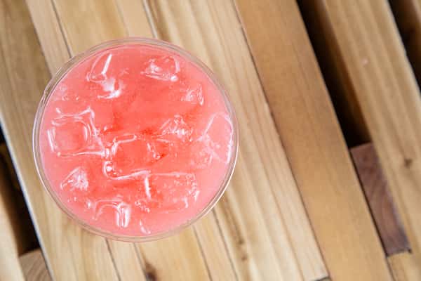Refreshing strawberry lemonade with a soft pink hue and ice cubes, captured from above on a wooden table, showcasing a bright and fruity summer café beverage.