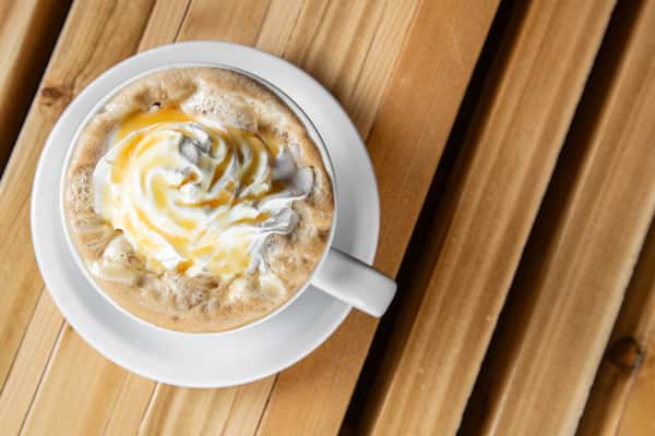 Hot white mocha topped with whipped cream and caramel drizzle in a white ceramic cup, served on a wooden table, highlighting a rich and cozy café-style beverage.