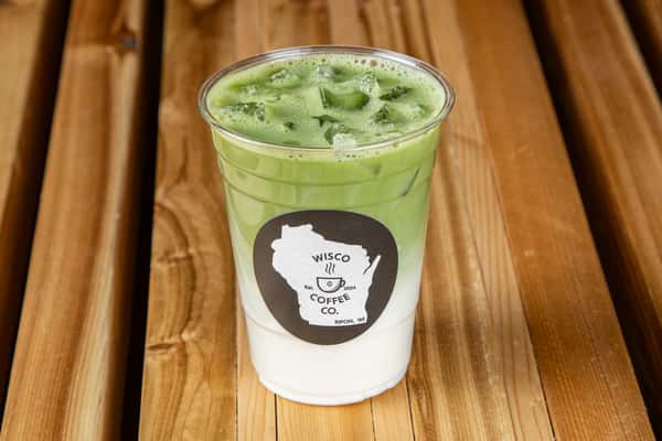 Iced matcha latte with layered milk and vibrant green tea foam in a clear cup on a wooden table, trendy café beverage
