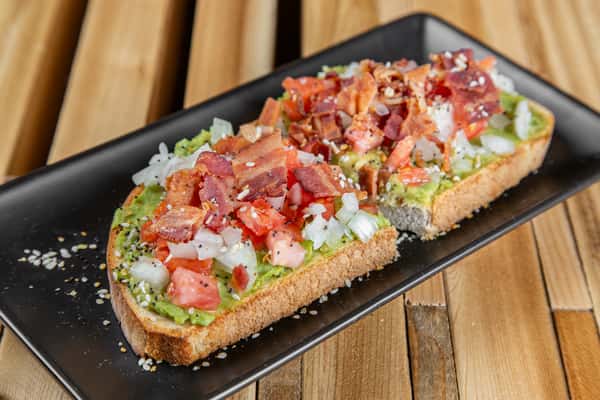 Avocado toast topped with bacon, tomatoes, and drizzle on artisan bread at Wisco Coffee Company