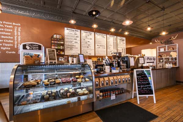 Modern coffee shop counter with pastry display, espresso bar, and menu boards, featuring warm lighting and a welcoming café environment.