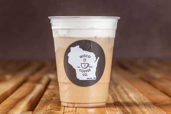 Iced vanilla white mocha latte with layered espresso and milk in a clear plastic cup, featuring a minimalist café logo, set on a rustic wooden table for a smooth, sweet coffeehouse drink.