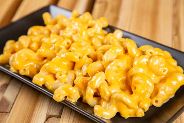 Creamy macaroni and cheese with rich, melted cheddar sauce on elbow pasta, served on a black tray over a rustic wooden table, highlighting a classic comfort food dish.