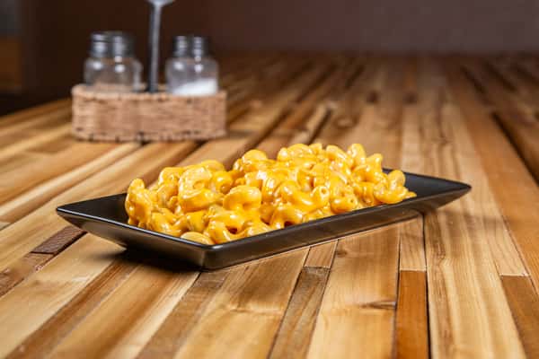 Creamy Wisconsin-style mac and cheese with rich melted cheddar sauce over elbow pasta, served on a black tray on a rustic wooden table, highlighting a classic comfort food dish.