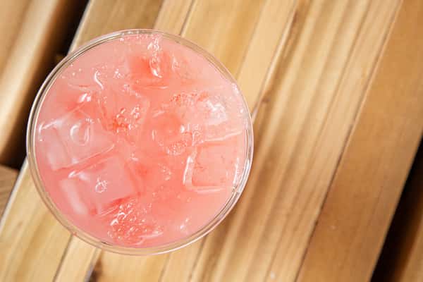 Refreshing strawberry lemonade with a soft pink hue and ice cubes, captured from above on a wooden table, showcasing a bright and fruity summer café beverage.
