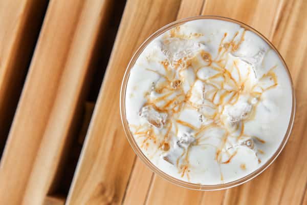 Iced white chocolate latte with creamy milk and espresso, topped with whipped cream and caramel drizzle, served in a clear cup on a rustic wooden table, highlighting a sweet and indulgent café-style drink.
