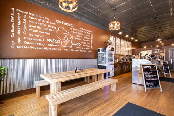 Rustic café interior with communal wooden seating, wall menu art, and warm pendant lighting, creating a cozy and inviting coffee shop atmosphere.