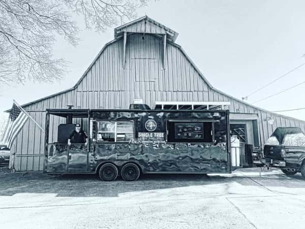 black and white photo of single tree food truck in front of barn