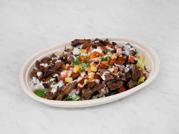 Bowl of grilled carne asada over a bed of lettuce and rice, topped with pico de gallo, corn, and drizzled with crema and salsa.