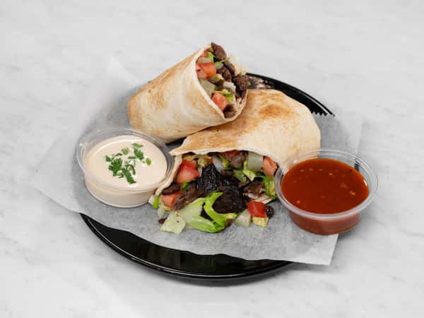 Grilled carne asada burrito cut in half, filled with lettuce, tomato, and onions, served with creamy chipotle sauce and spicy red salsa on a black plate.