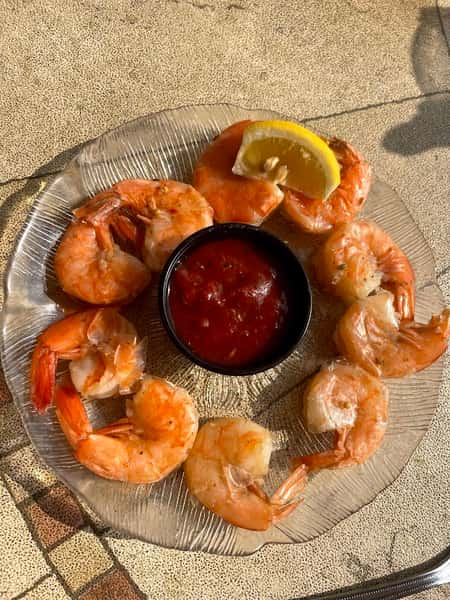 Fresh shrimp cocktail arranged around a dish of tangy cocktail sauce with a lemon wedge garnish, served on a clear glass plate.