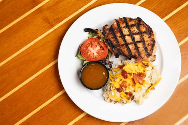 Grilled pork chop with crosshatch grill marks served with loaded mashed potatoes, brown gravy, and fresh greens.