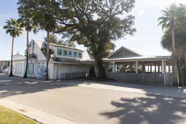 Side view of Bacchus seafood restaurant featuring palm trees, shaded patio seating, and beach-inspired architecture.