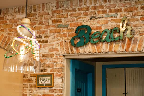 "Beach" sign mounted on exposed brick above a doorway, accented with beaded pendant lighting in a relaxed coastal restaurant interior.