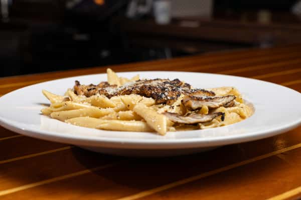 Creamy penne pasta topped with grilled chicken and cracked pepper, served on a white plate at a coastal dining restaurant.