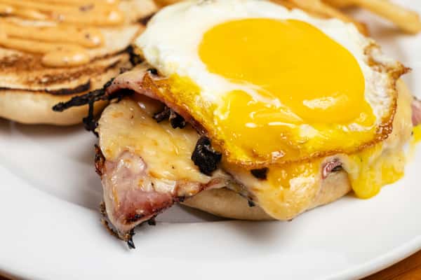 Breakfast sandwich with melted cheese, grilled ham, and a sunny-side-up egg on a toasted bun, served with fries at a casual coastal restaurant.