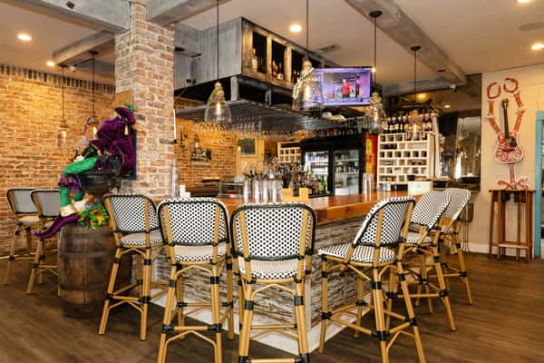Wide view of the Bacchus bar featuring exposed brick, hanging glassware, stocked liquor shelves, and festive décor for a vibrant seafood bar experience.