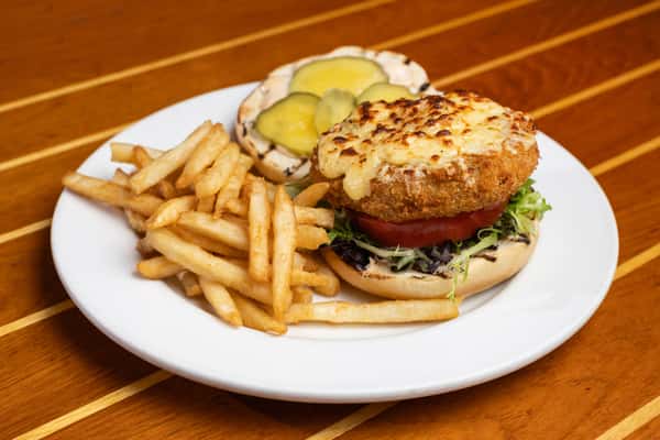 Golden crab cake sandwich topped with melted cheese, lettuce, and tomato, served with fries at a seafood restaurant.