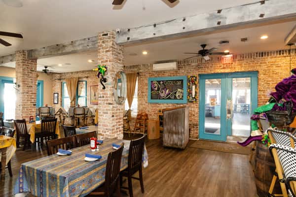 Rustic dining room with exposed brick walls, wooden beams, blue accents, and table seating, showcasing a cozy, homey bar and grill dining space.