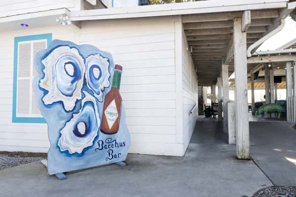 Painted oyster shell display with a hot sauce bottle and "Bacchus Bar" lettering outside a coastal seafood bar, highlighting playful Lowcountry decor.