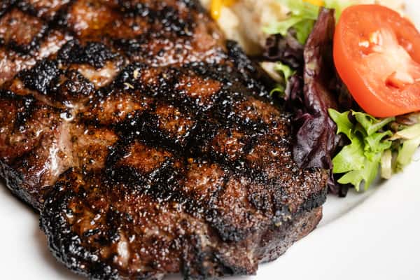 Close-up of a seasoned grilled pork chop with charred grill marks, paired with salad greens and sliced tomato.