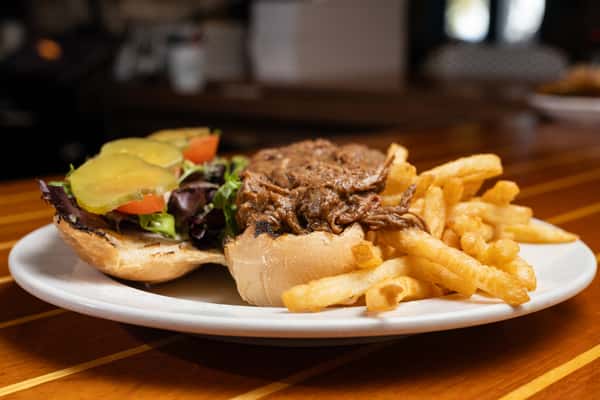 Open-faced roast beef sandwich with lettuce, tomato, pickles, and fries, served on a toasted roll.