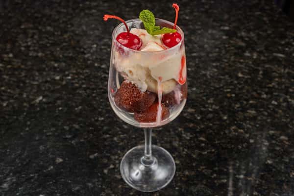 Gulab jamun with vanilla ice cream, cherries, and mint served in a dessert glass