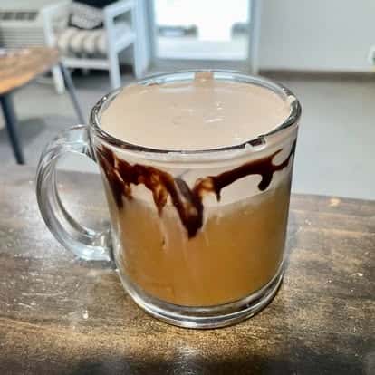 A ceramic mug of coffee with artistic cream and froth dripping down the sides, sitting on a wooden table.