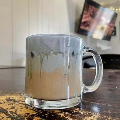 A ceramic mug of coffee with artistic cream and froth dripping down the sides, sitting on a wooden table.