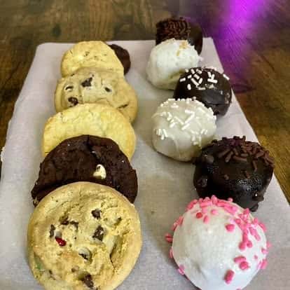 A tray of assorted cookies and chocolate-dipped treats, including chocolate chip cookies, cake balls, and pink-sprinkled items.