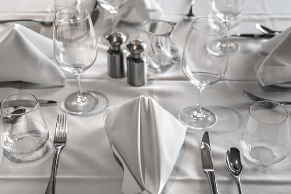 A pristine white table setting featuring transparent glass plates, glassware, and utensils, reflecting a modern and elegant dining aesthetic.
