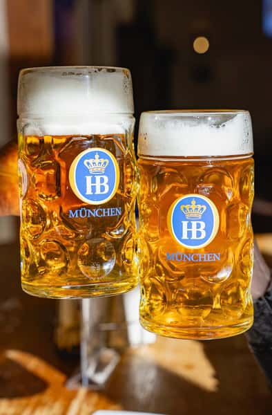 two large Hofbräu beer steins filled with golden lager on table