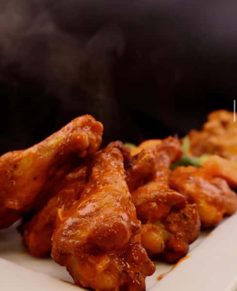 crispy chicken wings tossed in sauce served hot on a plate, bar food favorite
